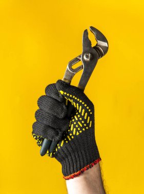 Usta bir tesisatçının inşaat eldiveninde kaldırılmış bir el sarı arka planda kerpeten tutuyor. Yenilemenin başarıyla tamamlandığının işareti