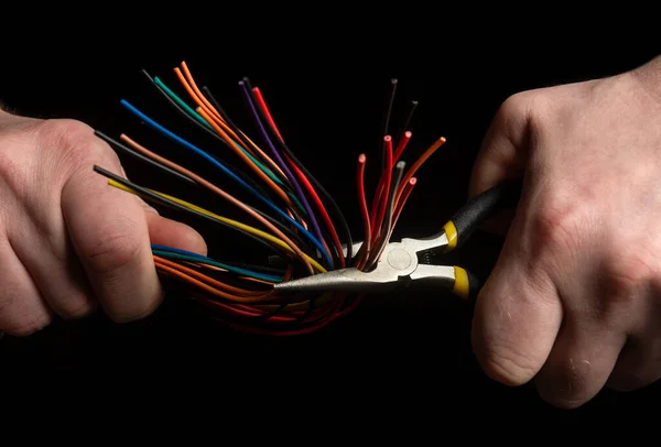 Hands of the master hold diagonal pliers and wire closeup on black background. Electronics Repair Idea