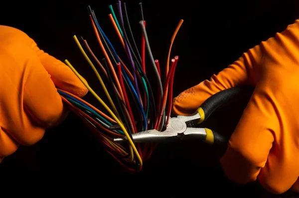 Hands in protective gloves of the master hold diagonal pliers and wire closeup on black background. Electronics Repair Idea
