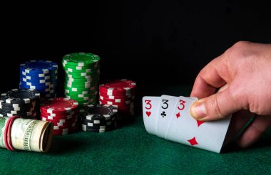 Poker kartları. Üçlü ya da set kombinasyonlu. Kumarbazın eli kumarhanede iskambil kağıdı tutar. Çipler yeşil masada.