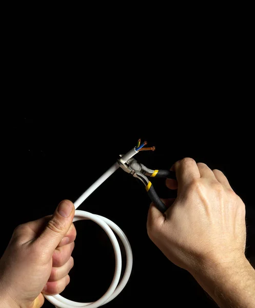 The electrician cuts the white cable with diagonal pliers. Hands of master close-up. Black isolated background