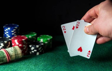 Poker kartları ve oyunda bir çift kombinasyon. Kumarbazın eli poker kulübünde iskambil kâğıdı tutuyor. Çipler yeşil masada.