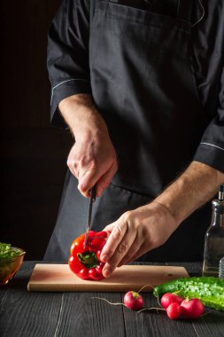 Kesme tahtasında biber kesen bir şefin yakın çekimi. Mutfakta, bir restoranda ya da kafede profesyonel salata hazırlığı. Dikey resim
