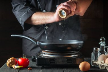 Şef tavada yumurta pişirirken biber ekler. Antika mutfak masasında çalışma ortamı