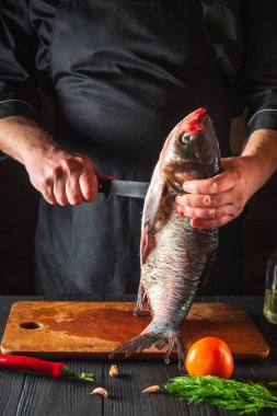Şef koca kafalı bir sazan balığını temizliyor. Restoranın mutfağında çalışma ortamı. Balık diyeti konsepti