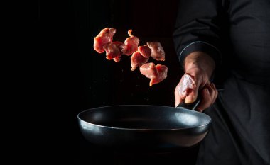 Profesyonel bir aşçının eli siyah arka planda et parçalarını kızartma tavasına fırlatır. Restoran yemekleri konsepti. Ücretsiz reklam alanı