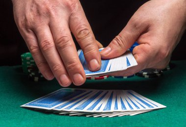 Bir poker kulübünün arka planında poker kartları karıştıran bir krupiyenin yakın çekim elleri, çipler. Poker ya da oyun işi konsepti