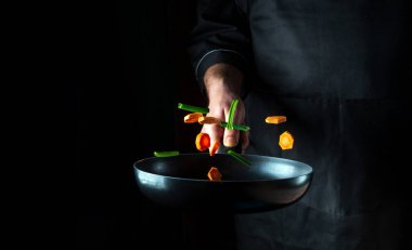 Profesyonel bir aşçının eli siyah arka planda sebze parçalarını kızartma tavasına atar. Restoran yemekleri konsepti. Bedava reklam spa 'sı
