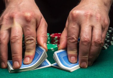 Bir poker kulübünün arka planında poker kartları karıştıran bir krupiyenin yakın çekim elleri, çipler. Poker ya da oyun işi konsepti