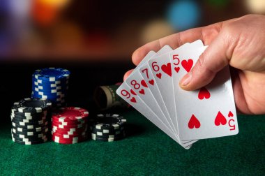  Oyunda floş kombinasyonu olan poker kartları. Kumarbazın eli poker kulübünde iskambil kâğıdı tutuyor. Fişler yeşil masaya.