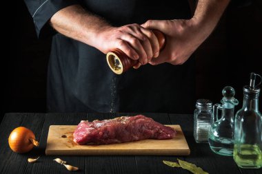 Şef çiğ et fileto pişiriyor ve siyah arkaplanda salamura yapmak için biber ve biber ekliyor. Restorandaki ya da kafedeki mutfakta çalışma ortamı