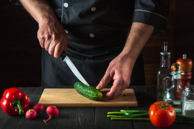 Profesyonel şef salata için mutfak masasında yeşil salatalık kesiyor. Sebze diyeti ya da abur cubur fikri.