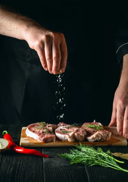 Chef or cook sprinkles the meat with salt. Preparing meat before baking. Working environment in kitchen of restaurant or cafe