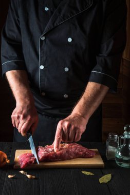 Şef mutfakta bıçakla et kesiyor, yemek pişiriyor. Mutfak masasındaki sebze ve baharatlar lezzetli bir öğle yemeği hazırlıyor.