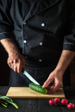 Profesyonel şef ya da aşçı salata için mutfak masasında yeşil salatalık kesiyor. Sebze diyeti ya da abur cubur fikri.