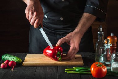 Profesyonel bir şef mutfak masasında salata için kırmızı biber kesiyor. Sebze diyeti ya da abur cubur fikri.