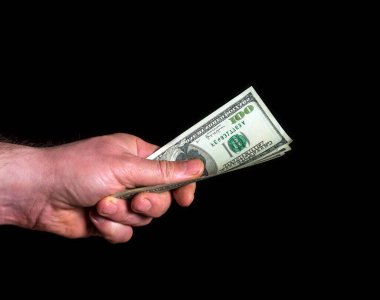 Siyah izole edilmiş arka planda dolarları elinde tutuyor. Başarı ve zenginlik fikri. Başarılı iş ve finans.