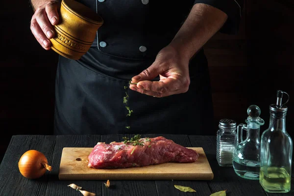 The chef prepares raw beef meat fillets and adds dry spices for the marinade. Working environment in the kitchen in a restaurant or cafe