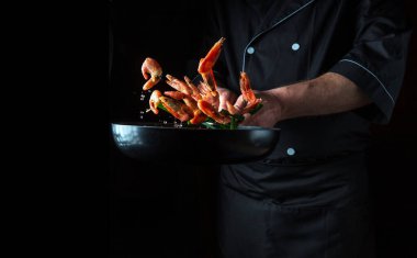 Profesyonel şef sebzeli tavada karides pişirir. Deniz ürünleri pişirmek, sağlıklı vejetaryen yiyecekler ve karanlık bir arka planda yemek. Hareket halindeyken donuyorum. Ücretsiz reklam alanı