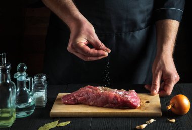 Şef ya da aşçı çiğ et ve tuz serpiyor. Pişirmeden önce sığır eti hazırlıyorum. Restoranın ya da kafenin mutfağında çalışma ortamı