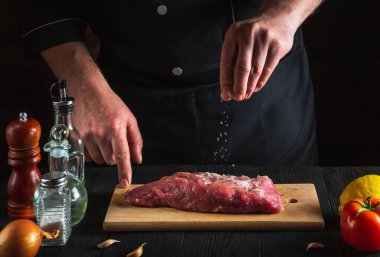 Profesyonel şef çiğ ete tuz serper. Pişirmeden önce et hazırlıyorum. Restoranın ya da kafenin mutfağında çalışma ortamı