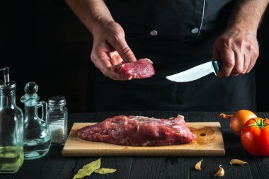 Aşçı, aşçı, mutfakta bıçakla et kesme, yemek pişirme. Mutfak masasındaki sebzeler ve baharatlar lezzetli bir öğle yemeği hazırlıyor.