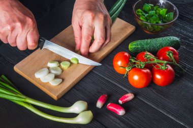Chef hands close-up cuts young green onions. Cooking salad in the restaurant kitchen. Set of vegetables for a salad diet.