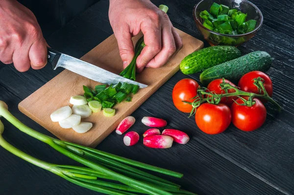 Chef hands close-up cuts young green onions. Cooking salad in the restaurant kitchen. Set of vegetables for a salad diet.