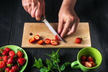 Şefin elleri naneli meşrubat yapmak için mutfak tahtasında taze çilek kesiyor..