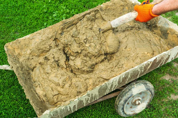 Master builder mixes the building mixture in cart for laying stone. Close-up of a builder is hand with a shovel during work