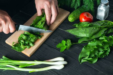 Profesyonel şef bir restoranda ıspanak salatası hazırlıyor. Kesme tahtasında bıçakla sebze kesen bir aşçının elleri..