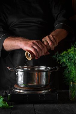 Şef börek yaparken tencereye biber ekliyor. Restorandaki klasik mutfak masasında çalışma ortamı. Dikey resim