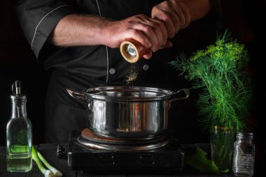 Şef börek yaparken tencereye biber ekliyor. Restorandaki klasik mutfak masasında çalışma ortamı