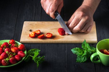 Şefin elleri naneli meşrubat yapmak için mutfak tahtasında taze çilek kesiyor. Yemek diyeti tatlısı.