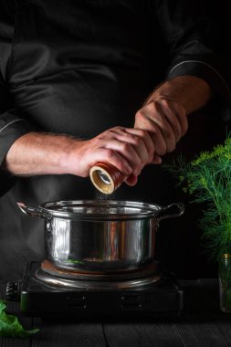 Şef börek yaparken tencereye biber ekliyor. Restorandaki klasik mutfak masasında çalışma ortamı. Dikey resim