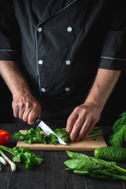 Bir şef bir restoran mutfağında ıspanak salatası hazırlar. Kesme tahtasında bıçakla sebze kesen bir aşçının elleri..