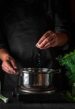 Şef börek yaparken tencereye tuz ekler. Restorandaki klasik mutfak masasında çalışma ortamı. Dikey resim.