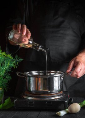 Profesyonel şef börek yaparken tencereye yağ ekliyor. Restorandaki klasik mutfak masasında çalışma ortamı. Dikey resim