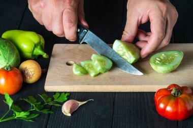 Bir restoranın mutfağında, bir şef salata için olgun bir salatalık kesiyor. İş sırasında aşçının ellerini yakın plan çek.