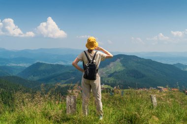 Şapkalı ve sırt çantalı gezgin doğada dinleniyor. Bir turist kız dağların manzarasına bakar. Dağ güzel manzara