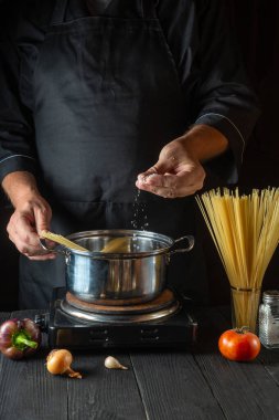 Restoranın mutfağında İtalyan spagettisi pişirmek. Şef bir kap kaynar suya tuz ekliyor. Dikey resim