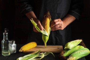 Profesyonel şef pişirmeden önce olgun mısırı kabuğundan soyar. Restoranın mutfağında çalışma ortamı. Çalışırken aşçının elleri....