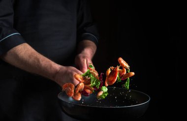 Aşçı ya da şef sebzeli tavada karides pişirir. Deniz ürünleri pişirmek, sağlıklı vejetaryen yiyecekler ve karanlık arka planda yemek. Hareket halindeyken donuyorum. Ücretsiz reklam alanı