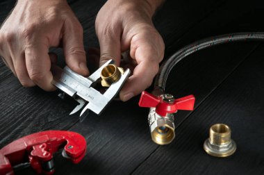 Büyücü, su ya da gaz borusunu bağlamadan önce kalibrenin boyutunu ölçer. Usta muslukçunun ellerine yakın çekim