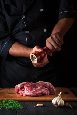 Profesyonel şef çiğ et fileto pişiriyor ve siyah arka planda salamura için biber ya da biber ekliyor. Restoranda ya da kafede, mutfakta çalışma ortamı