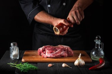 Profesyonel şef çiğ et fileto pişiriyor ve siyah arka planda salamura için biber ya da biber ekliyor. Restoranda ya da kafede, mutfakta çalışma ortamı