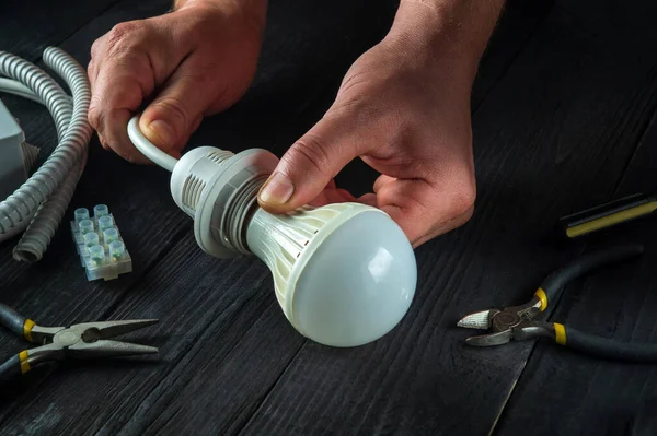 The master electrician turns on the light bulb. Close-up of worker hands on a work table in a workshop during work