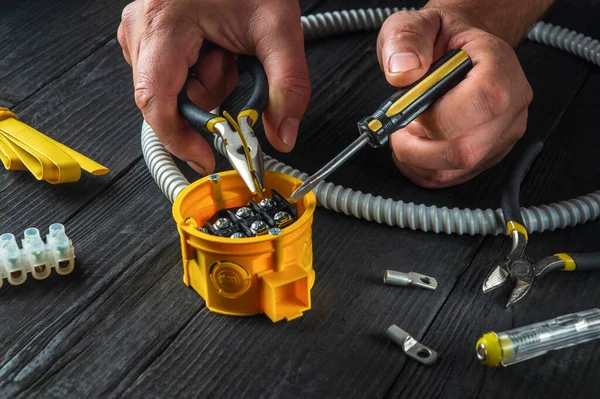 Electrical connection in the workshop of a master electrician. Close-up of hands of a master electrician during work. Installing a cable or wire to yellow junction box. Free advertising space