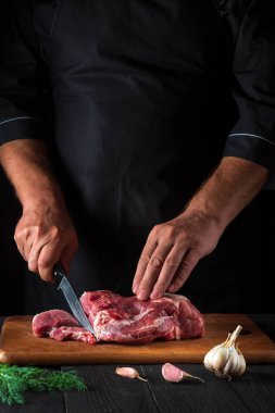 Şef mutfakta bir bıçakla et keser ve yemek hazırlar. Bir restoranda lezzetli bir öğle yemeği hazırlamak için mutfak masasındaki sebze ve baharatlar..