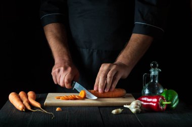 Şef, restoranın mutfağında sebze çorbası için havuç kesiyor. İş sırasında aşçının ellerini yakın plan çek. Havuç öldü.